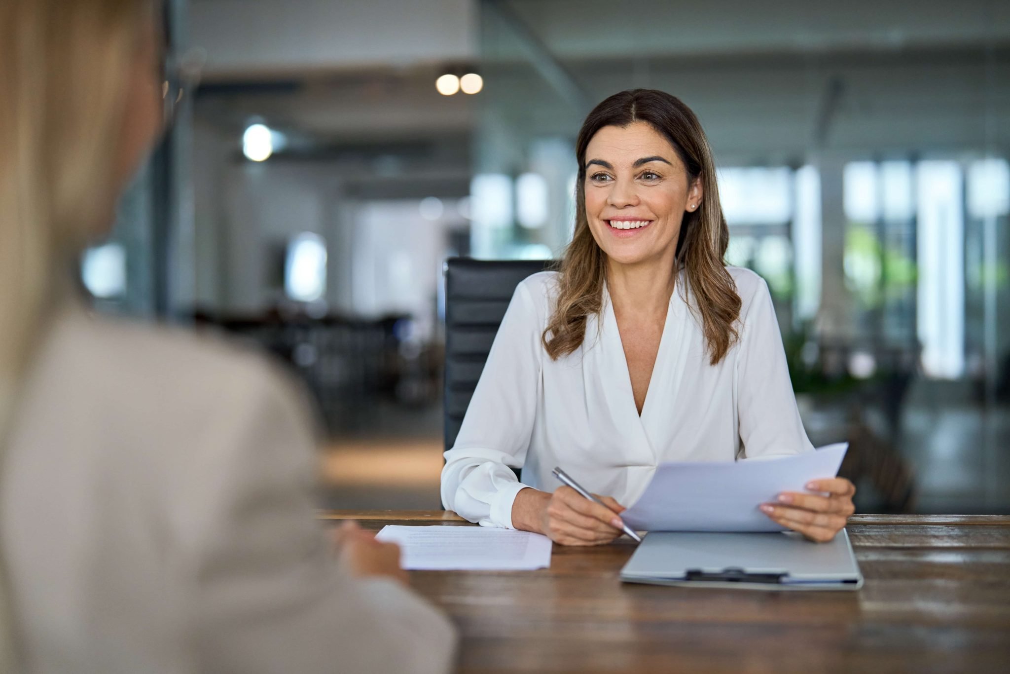 Smiling hr manager conducting a job interview with a female applicant sitting across the desk in an office meeting room.