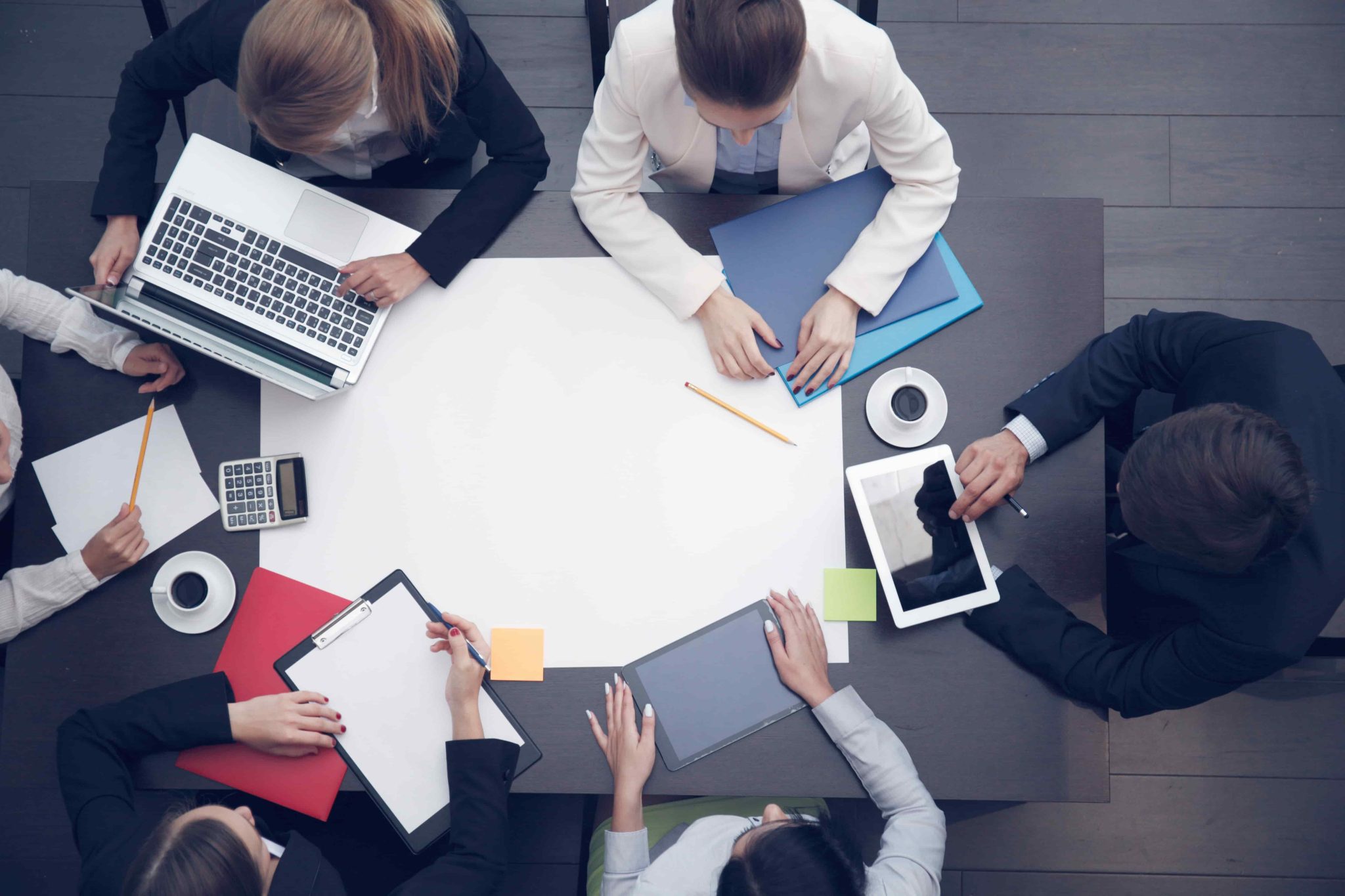 Top down view of multiple people sat around a table with laptops and paper having a discussion.