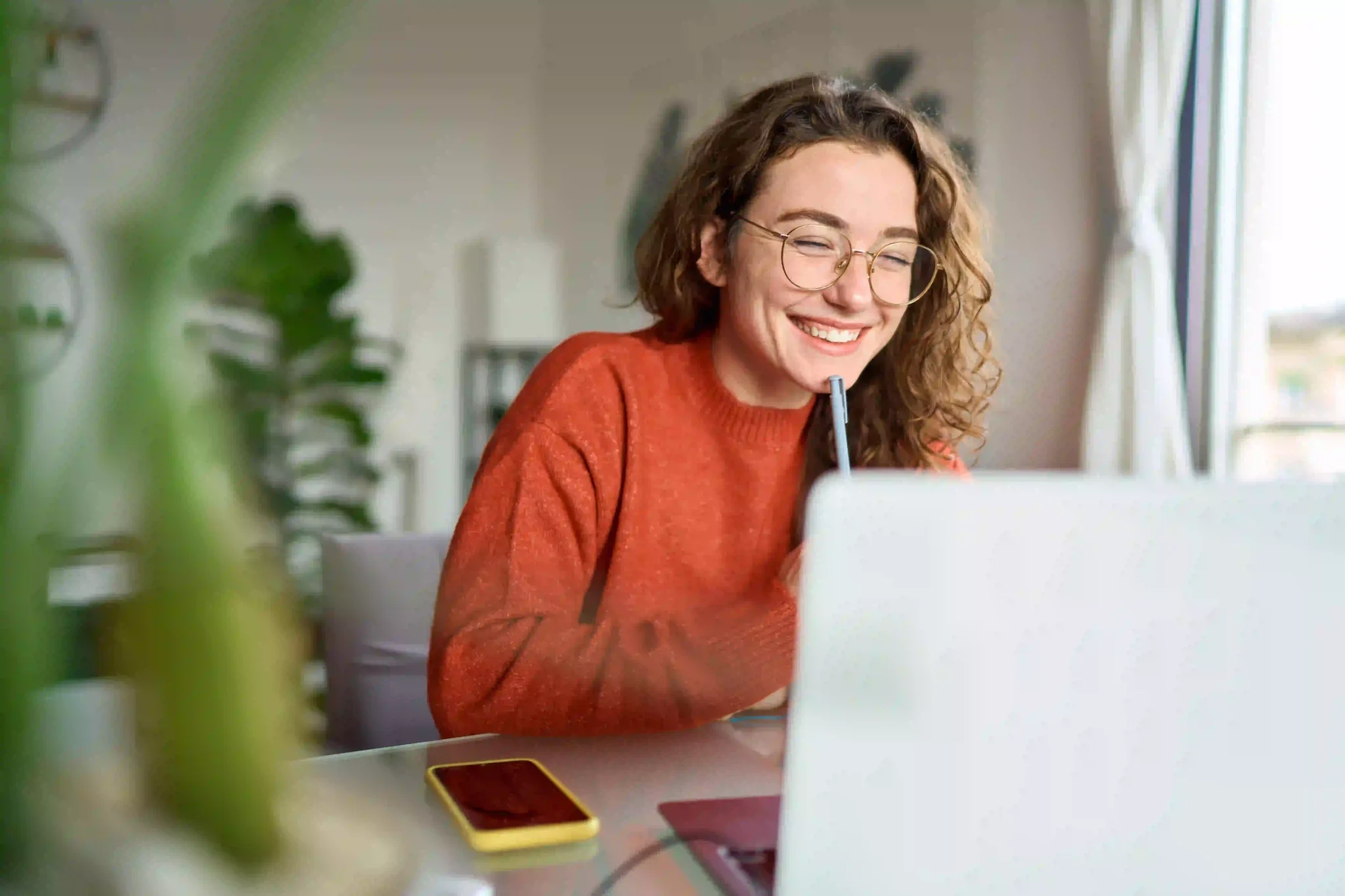Happy young woman using laptop sitting at desk writing notes while remote working
