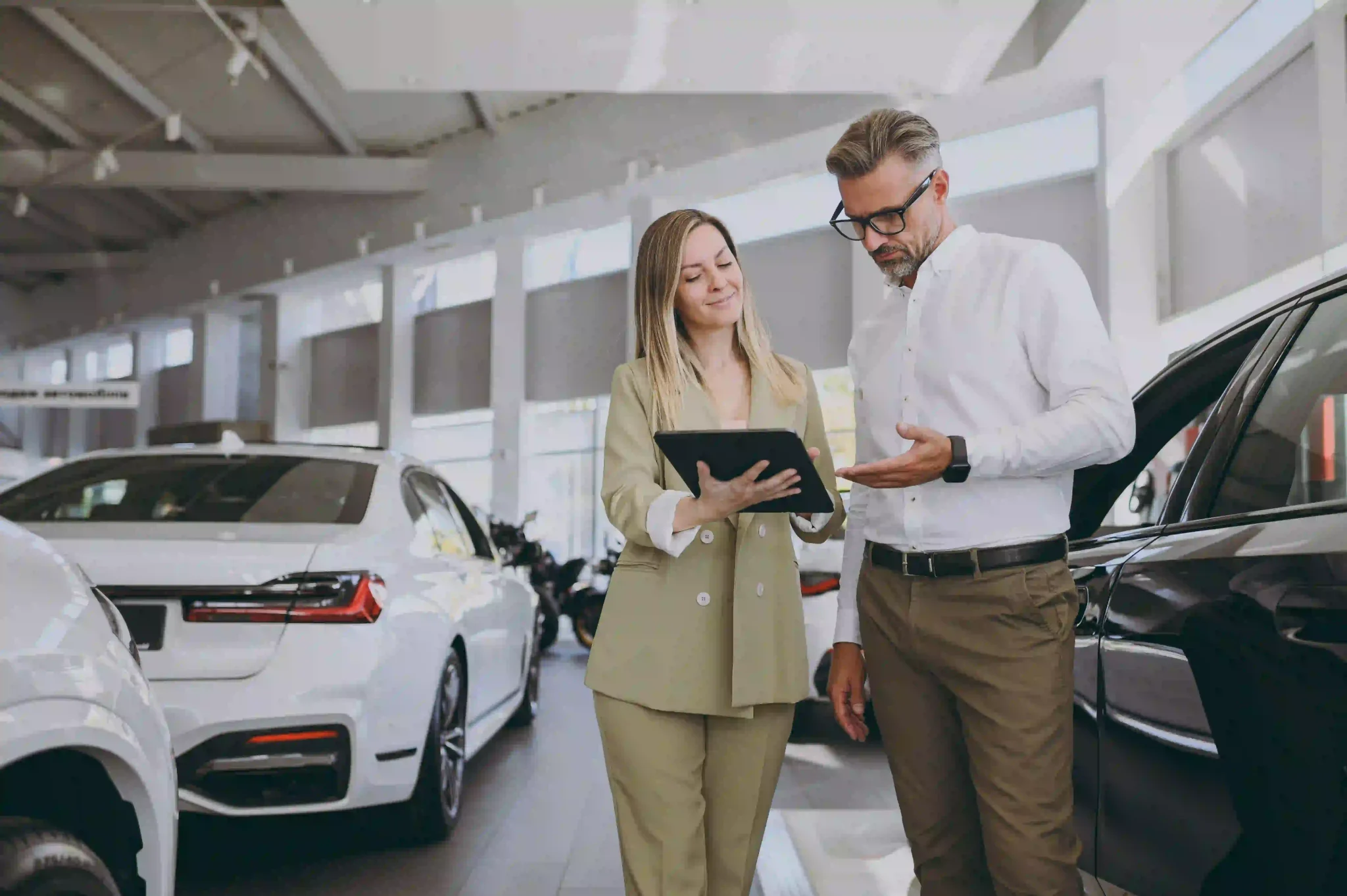 Two people in a car showroom, looking at documents on a tablet