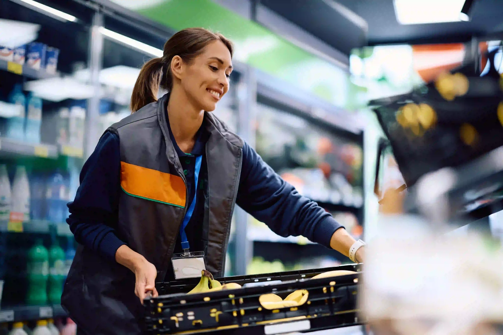 Happy supermarket employee working at fresh fruit section at the store.