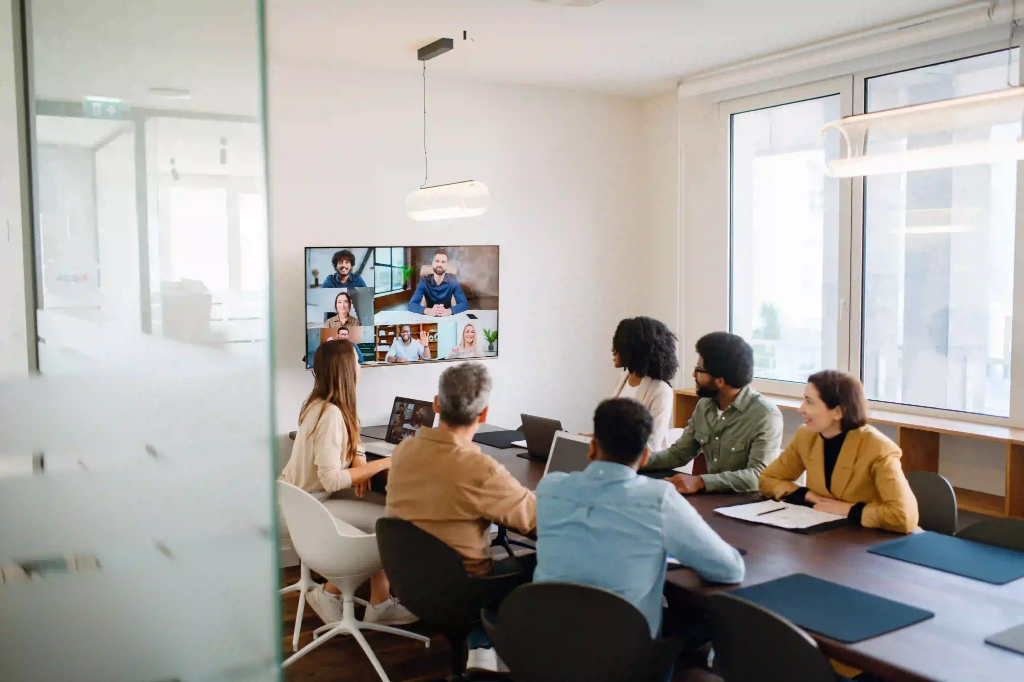 A team actively engages with remote colleagues via a large screen, illustrating the modern hybrid work model.