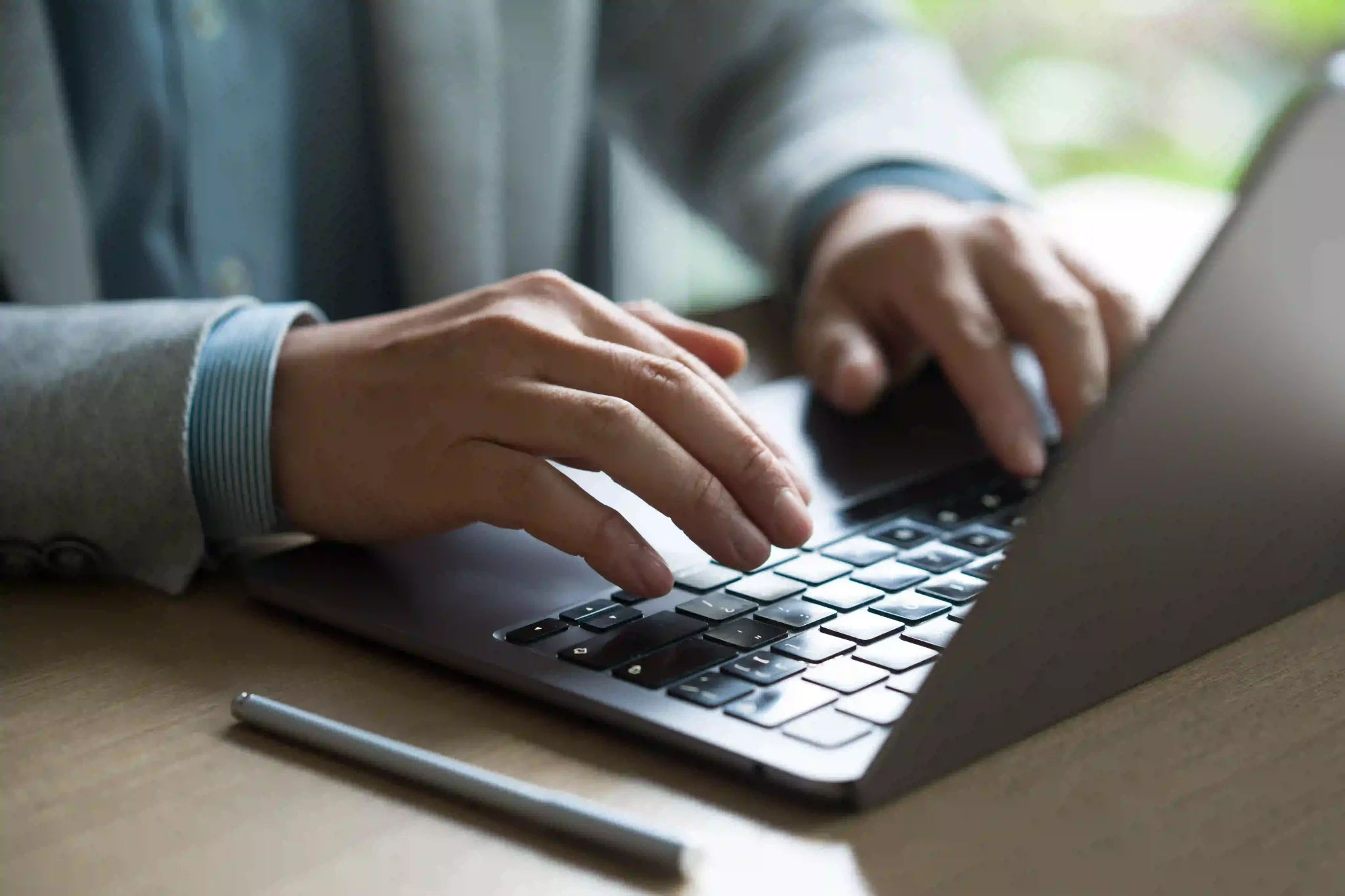 Man in grey suit sat at a desk typing on a laptop.